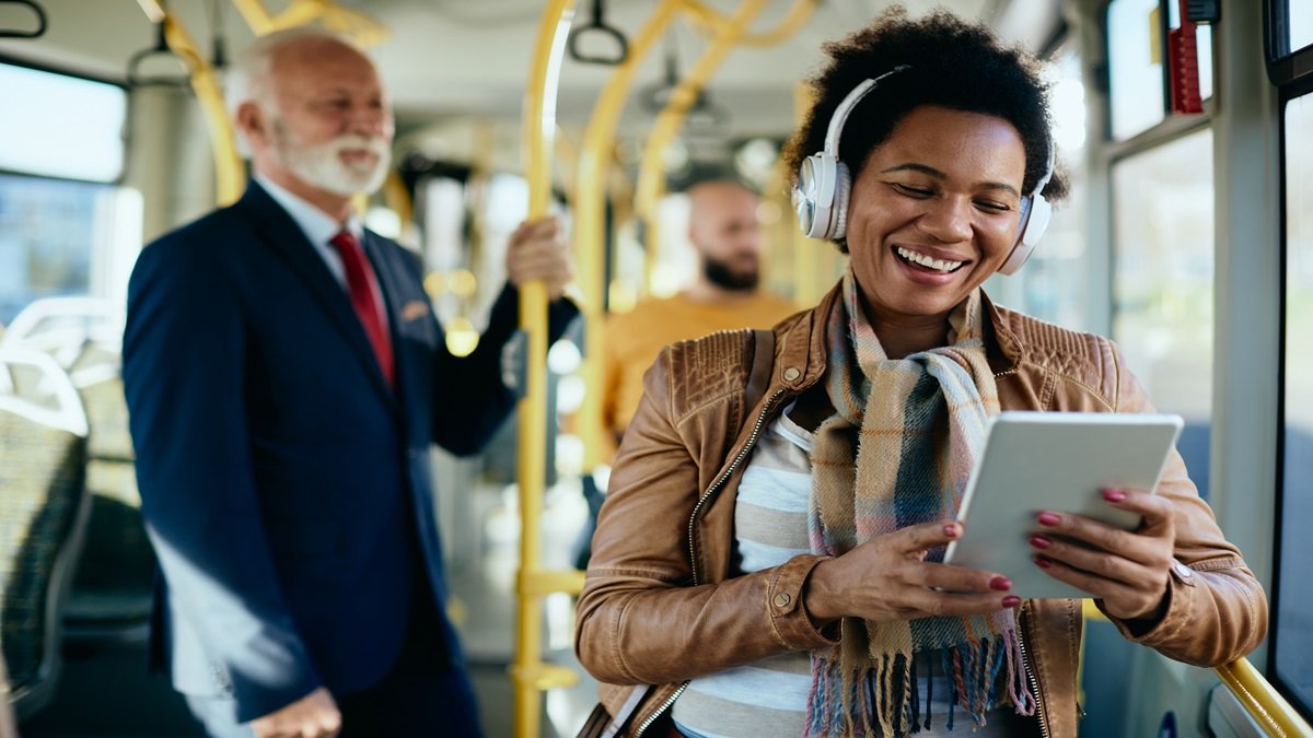 Jovem concentrado usando fones de ouvido e um tablet em um ônibus urbano.